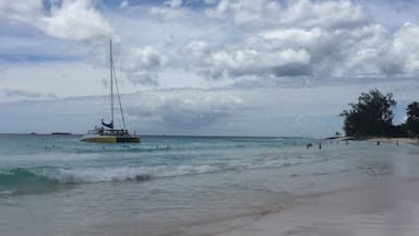 Uma praia com um veleiro na água e pessoas nadando.