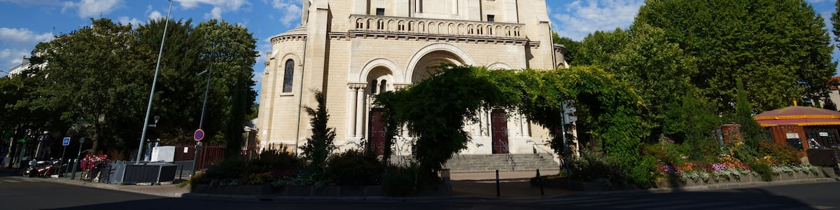 A large church with a tall bell tower, surrounded by trees and a clear blue sky.
