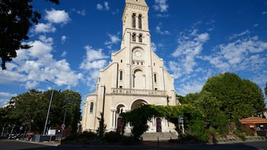 Uma igreja grande com uma torre de sino alta, rodeada por árvores e um céu azul límpido.