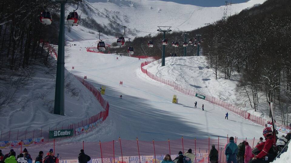 A ski slope with a ski lift, a crowd of people, and a snow-covered mountain.