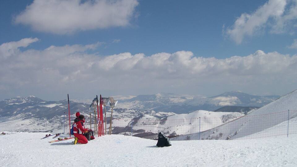 A snowy mountain landscape with a clear sky, ski equipment, and a red safety net.