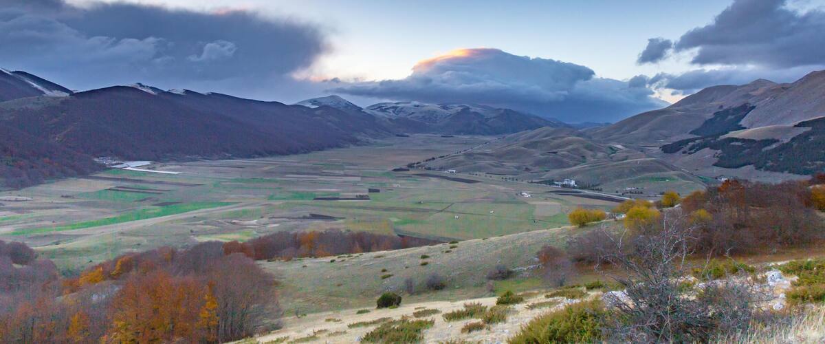 A valley with mountains, a river, and autumn-colored trees.
