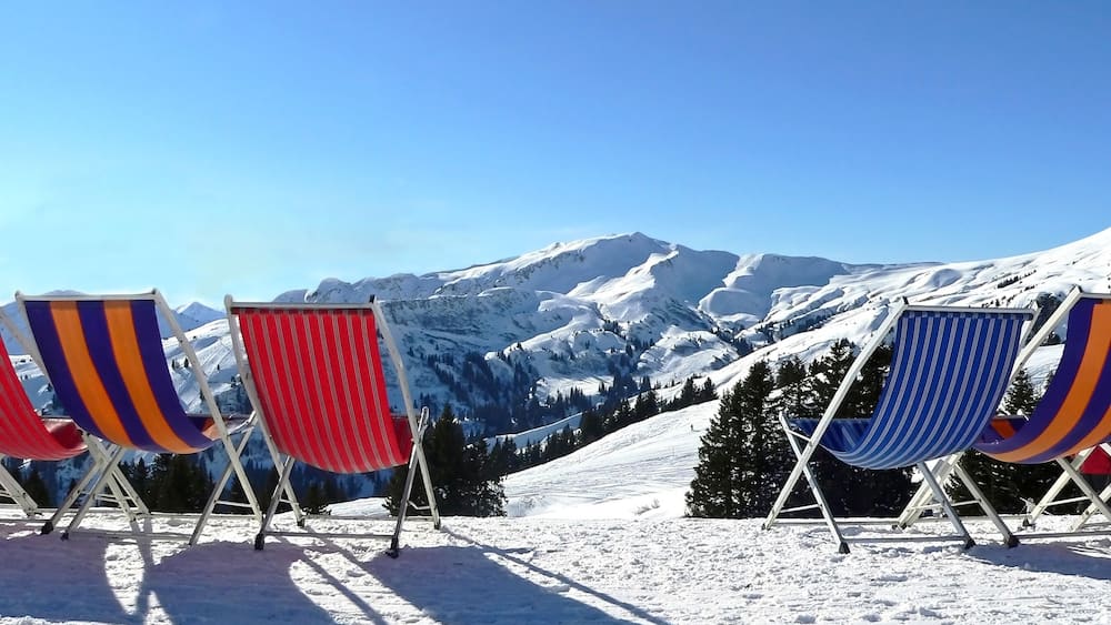 Vier Strandstühle mit bunten, gestreiften Kissen an einem verschneiten Berghang.