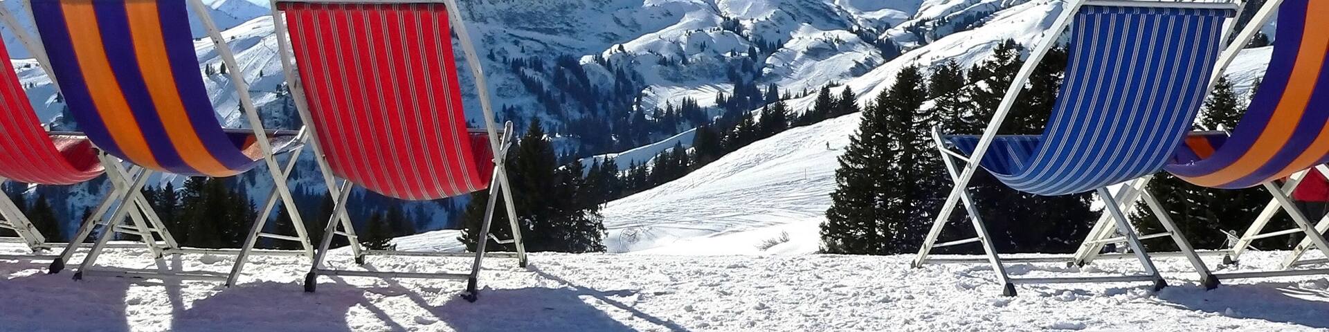Four beach chairs with colorful striped cushions on a snowy mountain slope.