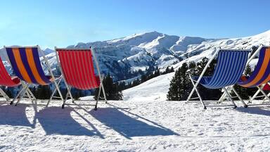 Four beach chairs with colorful striped cushions on a snowy mountain slope.