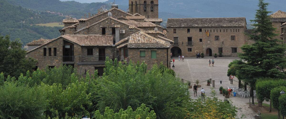 A historic town with a prominent tower, cobblestone streets, and lush greenery.