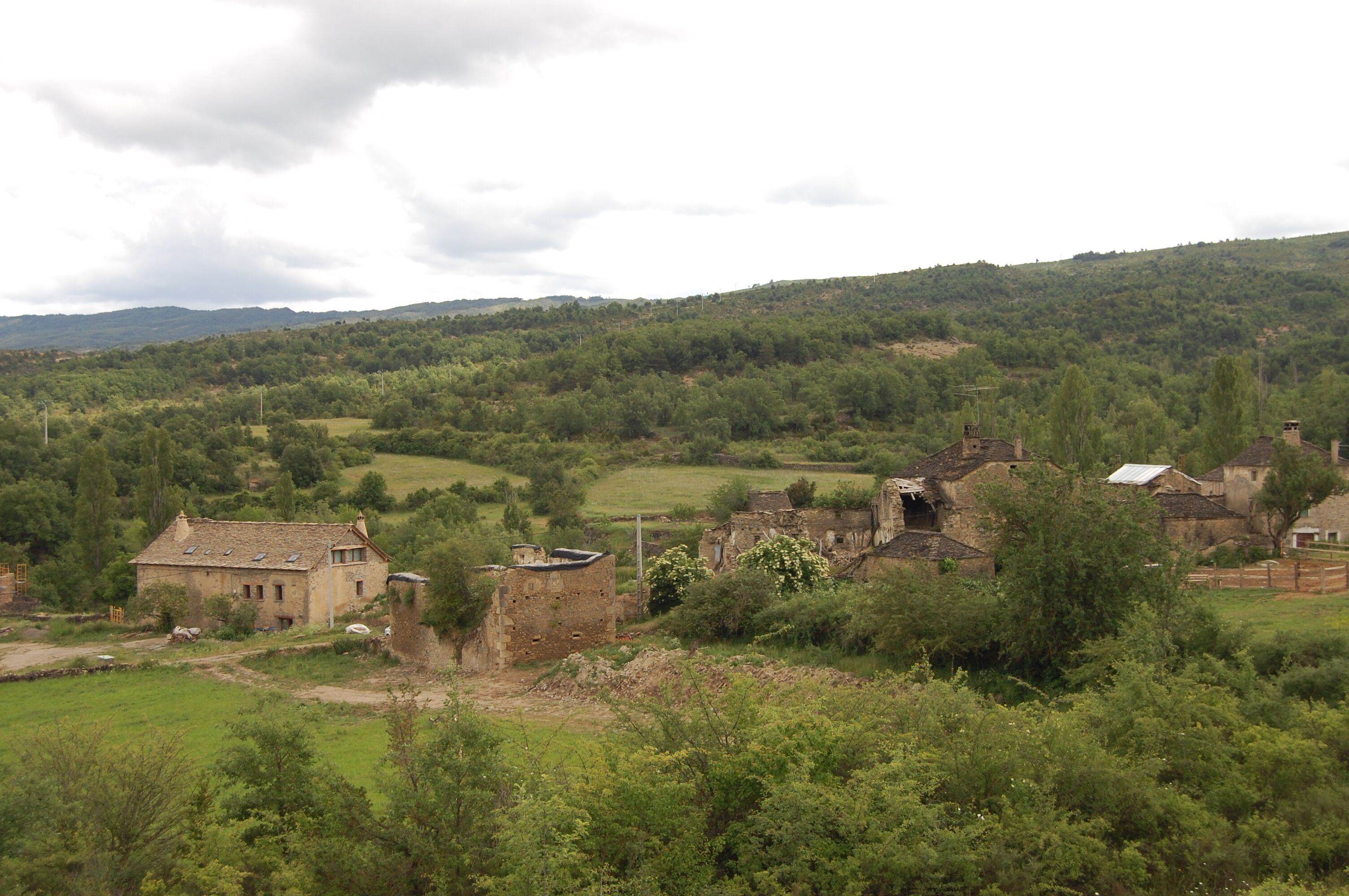 A rural landscape with a stone house, a barn, and rolling hills in the background.