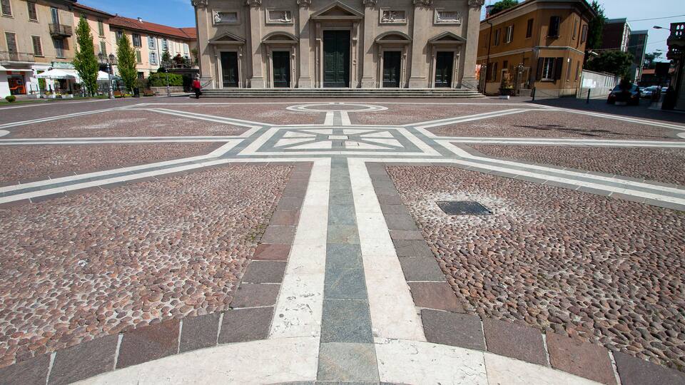 A plaza with a geometric tile pattern and a large building with classical architecture in the background.