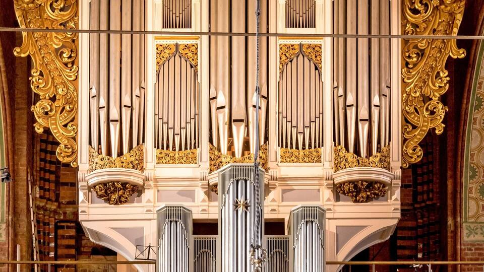 An ornate organ with gold detailing and a chandelier.