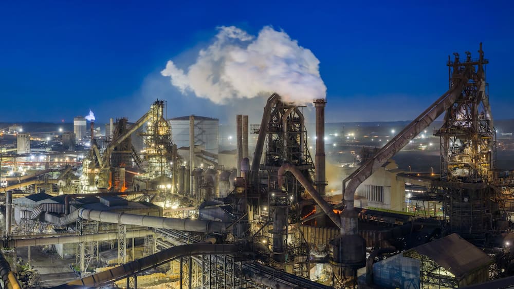 An industrial complex with multiple smokestacks, large processing towers, and extensive piping networks.