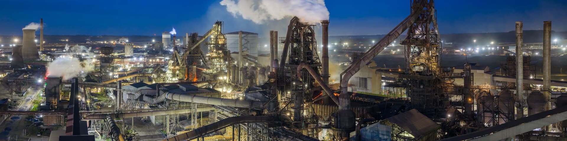 An industrial complex with multiple smokestacks, large processing towers, and extensive piping networks.