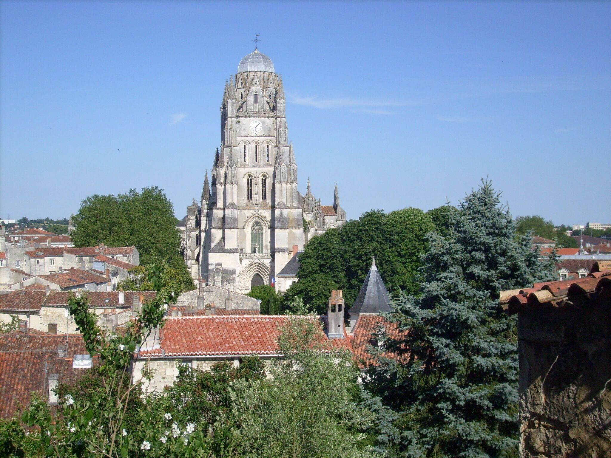A Gothic cathedral with a tall spire, surrounded by red-tiled roofs and greenery.