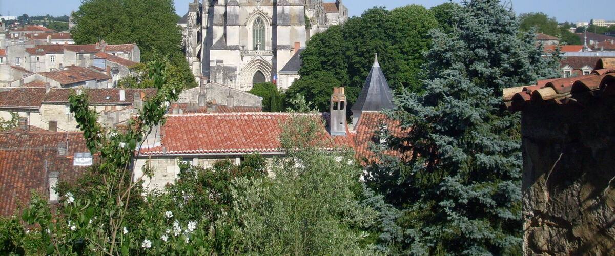 A Gothic cathedral with a tall spire, surrounded by red-tiled roofs and greenery.