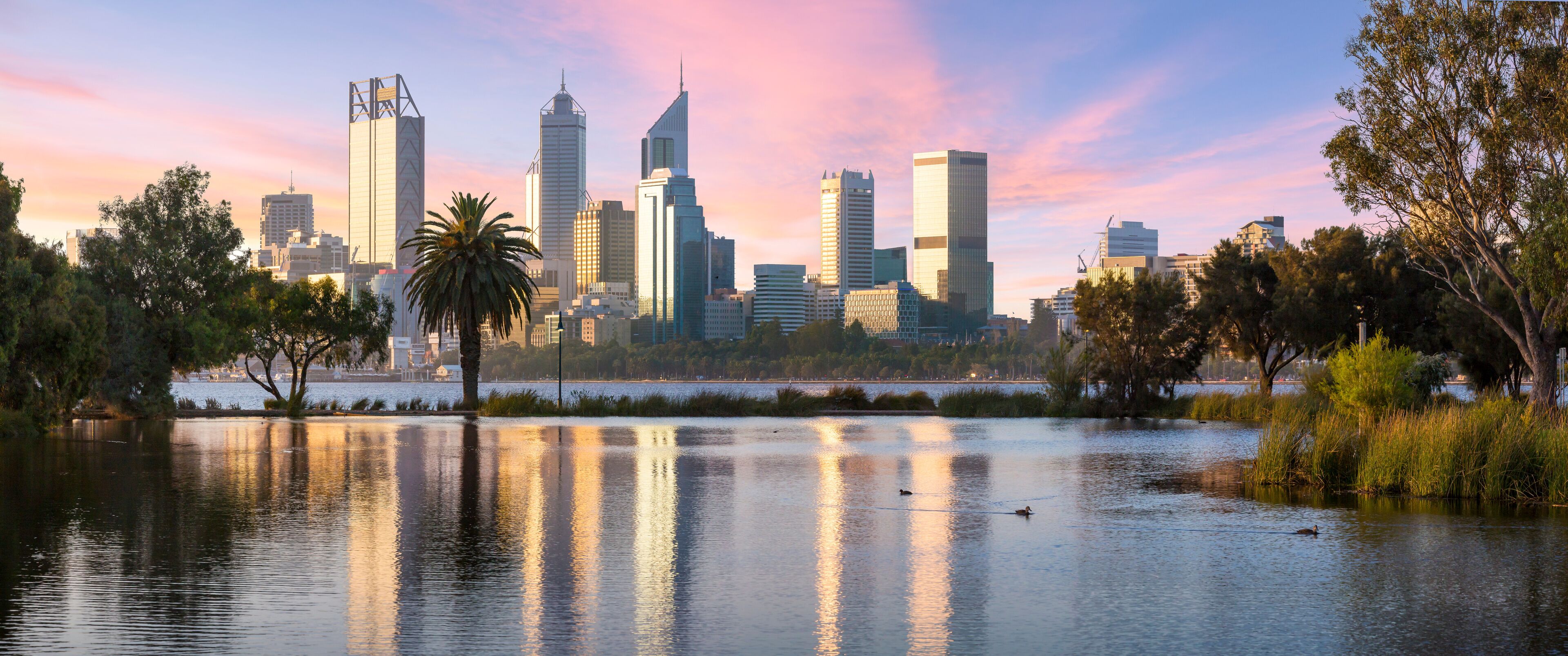 Un horizonte urbano con rascacielos modernos y un lago tranquilo que refleja los edificios.