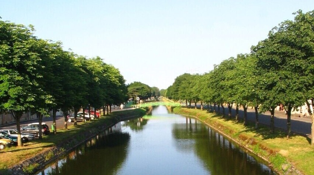 Canal de Berry à Saint-Amand Montrond, Cher, vue O-E. Aménagé entre début et mi-XIXe s. au petit gabarit berrichon (27,5 x 2,6 m, port max. 60 t), il est déclassé en 1955. On est loin des dimensions Freycinet, 38,5 x 5,05 m, port de 250 à 400 t, normes d’une grande part du réseau fluvial français, un peu plus tard ! Ses 3 branches cumulées, représentent 320 km de voies d’eau. Celle traversant la ville, dite sud et qui opère un large coude, vient de Montluçon, Allier.