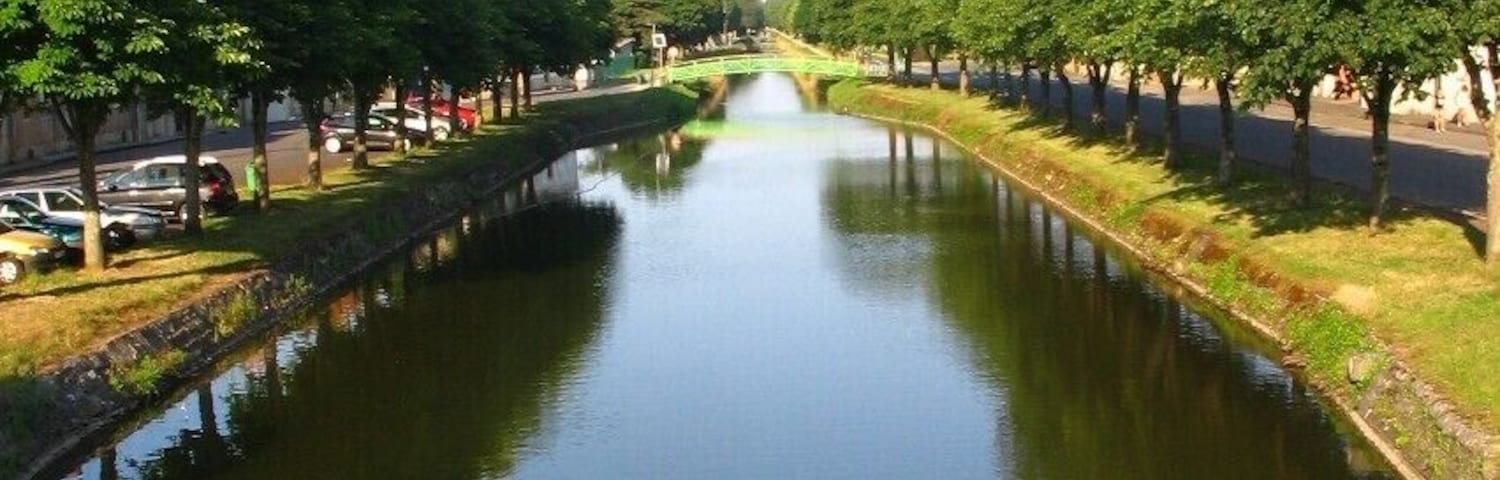 Canal de Berry à Saint-Amand Montrond, Cher, vue O-E. Aménagé entre début et mi-XIXe s. au petit gabarit berrichon (27,5 x 2,6 m, port max. 60 t), il est déclassé en 1955. On est loin des dimensions Freycinet, 38,5 x 5,05 m, port de 250 à 400 t, normes d’une grande part du réseau fluvial français, un peu plus tard ! Ses 3 branches cumulées, représentent 320 km de voies d’eau. Celle traversant la ville, dite sud et qui opère un large coude, vient de Montluçon, Allier.