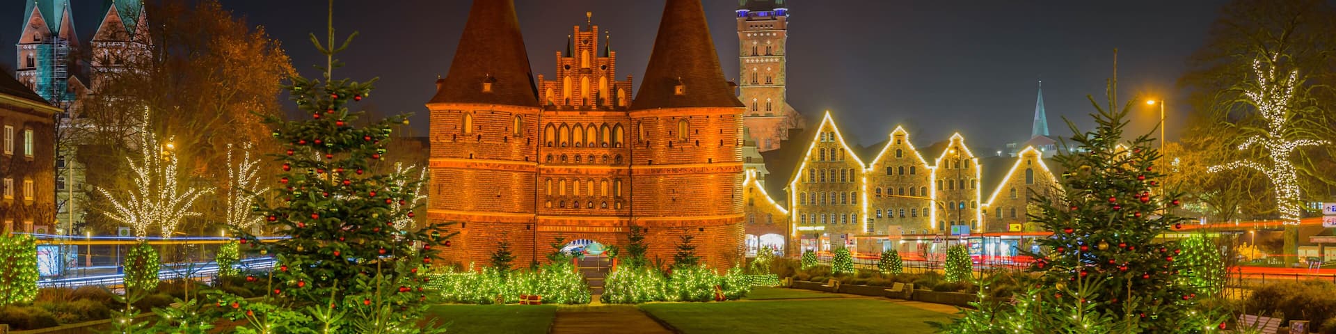 View of festive lighting and Christmas romantic atmosphere in the Hanseatic city of Lübeck at night. Nighttime view of Holsten Gate at Christmas time. Christmas tree with gifts.Christmas city.