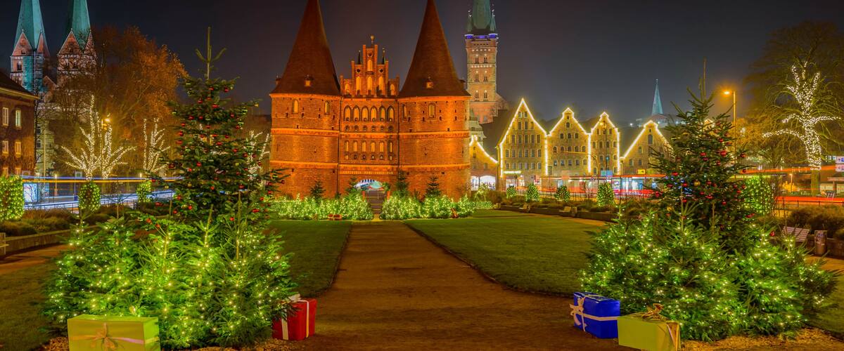 A historic building with three spires, surrounded by Christmas trees and illuminated lights.