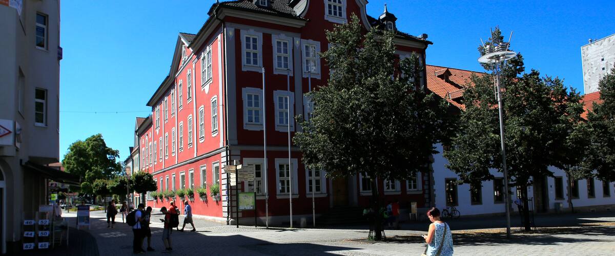 A red building with a clock tower, cobblestone street, and a clear blue sky.