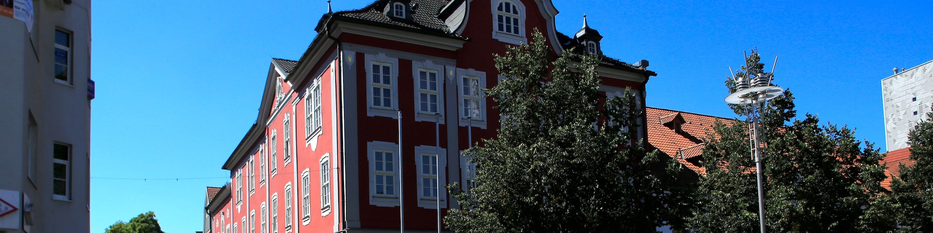 A red building with a clock tower, cobblestone street, and a clear blue sky.