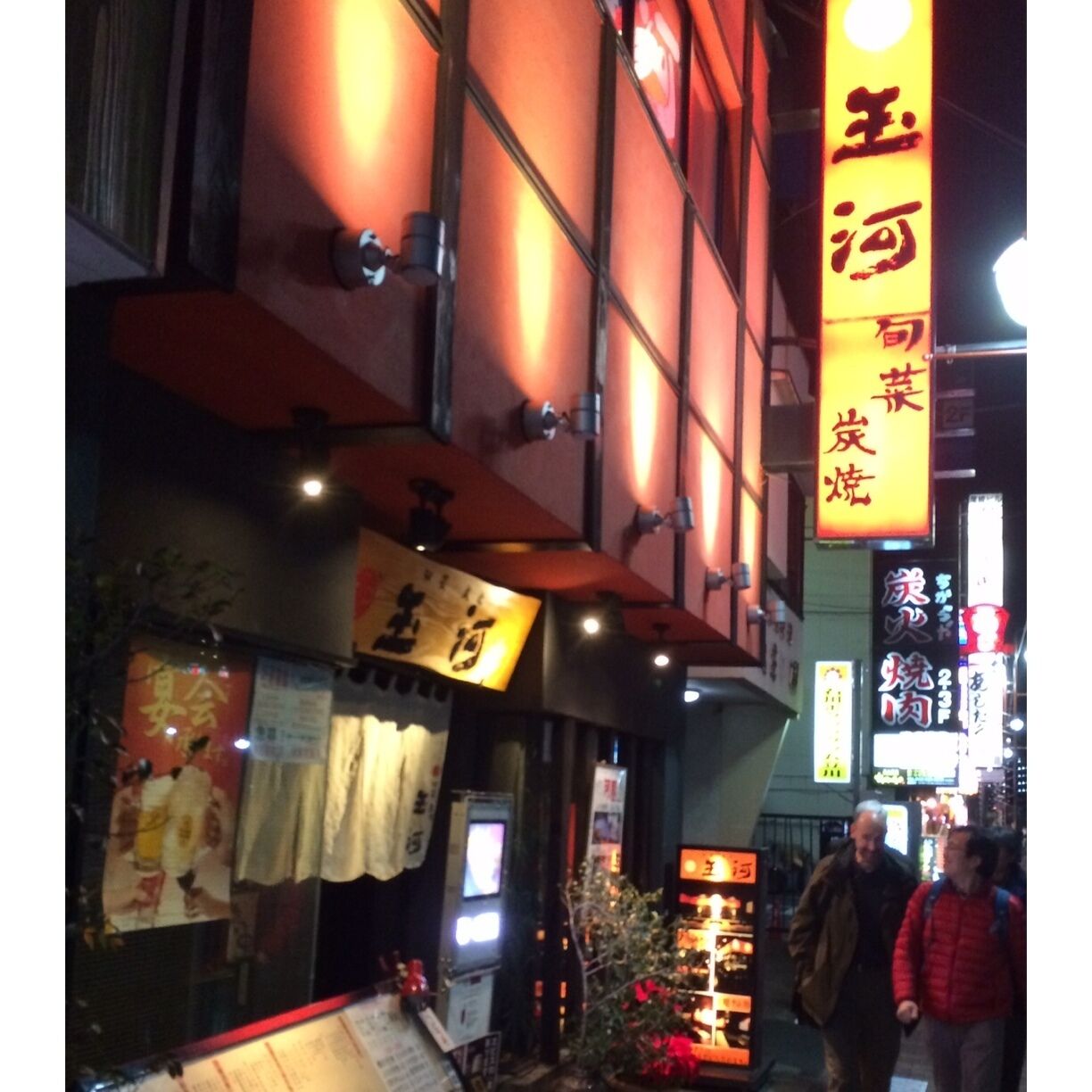 Fachada luminosa com grandes caracteres chineses e uma placa.