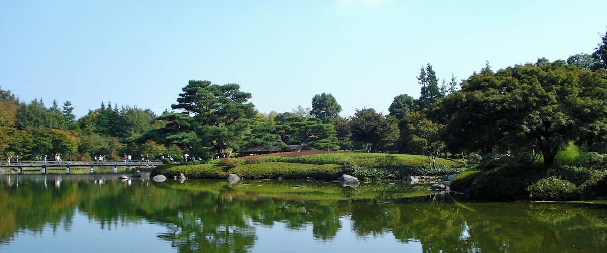 A calm lake with reflections of trees and a bridge.
