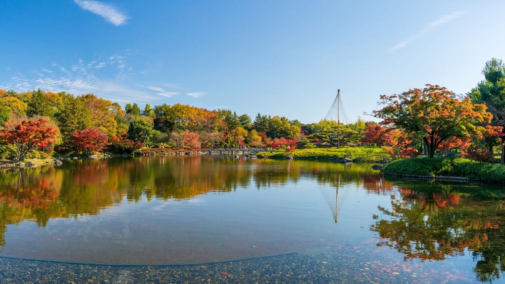 A serene lake with autumn foliage, a bridge, and a pagoda in the background.