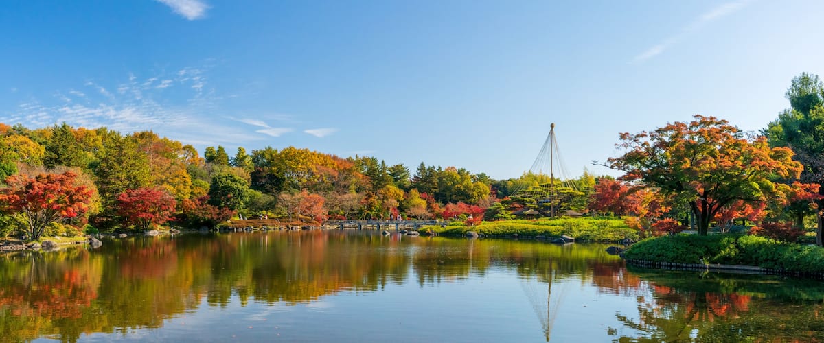A serene lake with autumn foliage, a bridge, and a pagoda in the background.