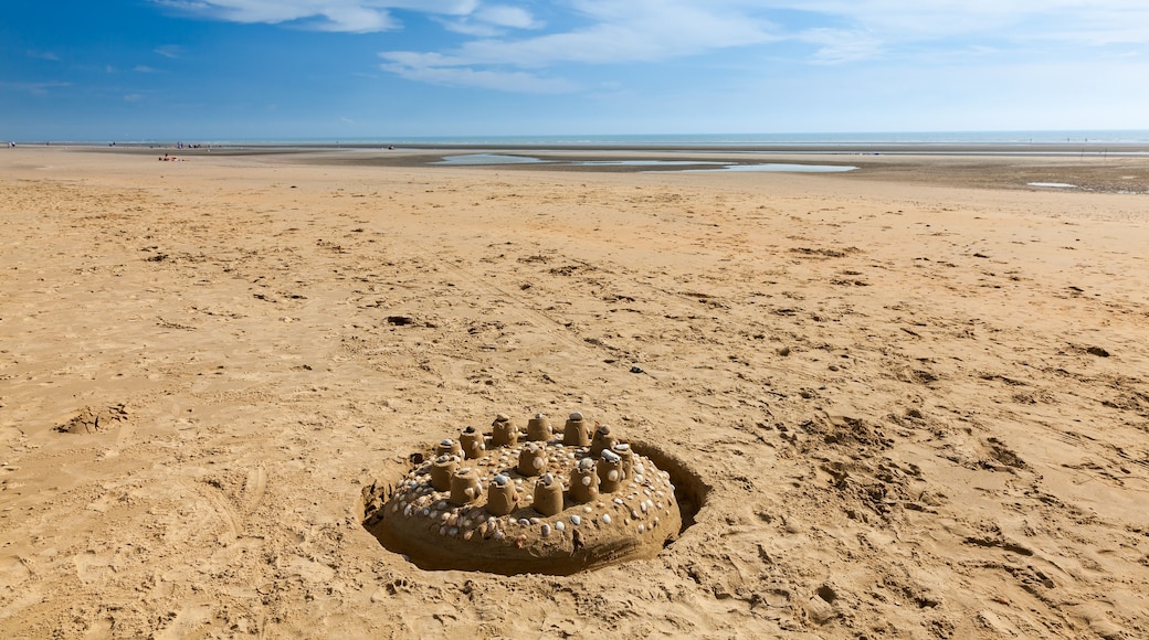Een zandstrand met een groot zandkasteel op de voorgrond en een rustige zee op de achtergrond.