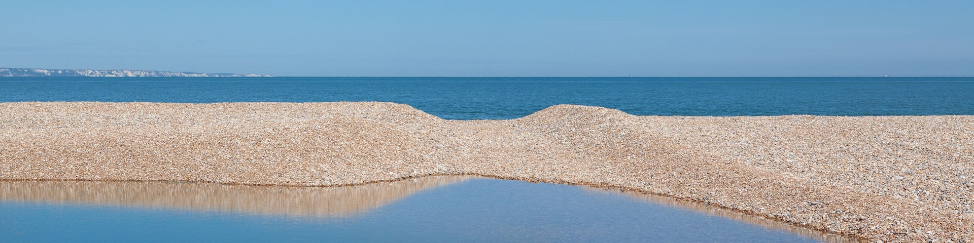 A pebbly beach with calm water reflecting the sky.
