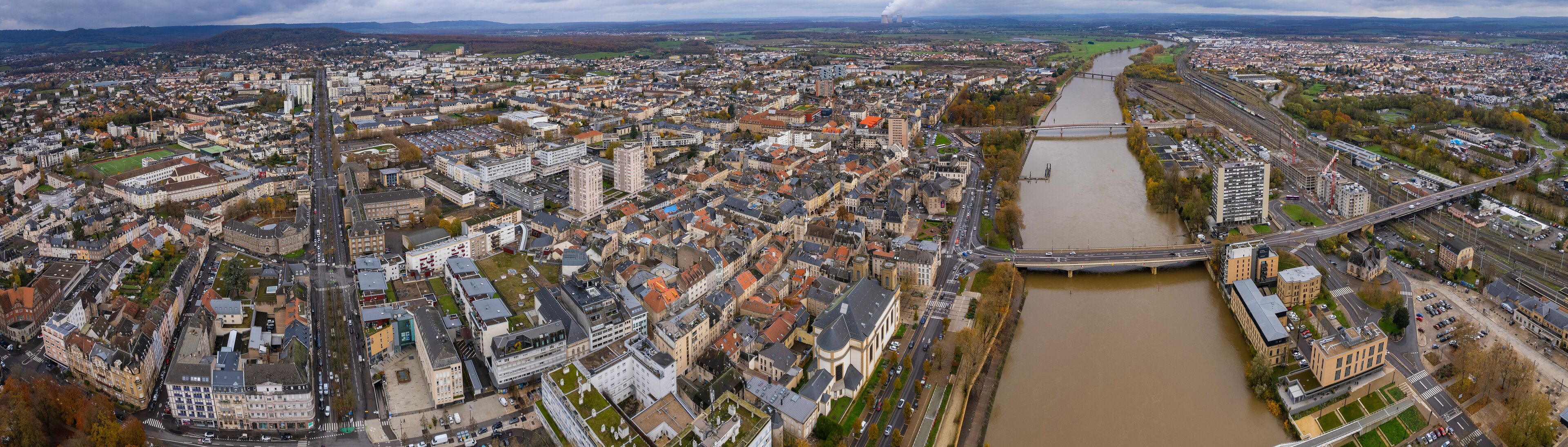 An aerial view of a densely populated city with a river running through it, a bridge crossing the river, and a railway line parallel to the river.