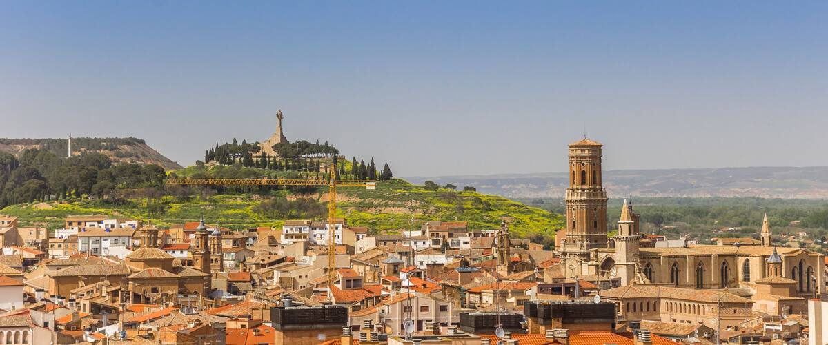 A historic town with a prominent church tower and a statue on a hill.