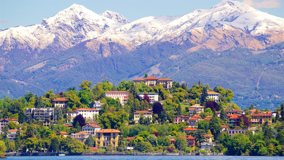 A coastal town with buildings on a hillside, a body of water in the foreground, and snow-capped mountains in the background.