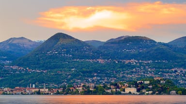 Paisagem montanhosa com uma cidade na base, um corpo d'água em primeiro plano e um pôr do sol ao fundo.