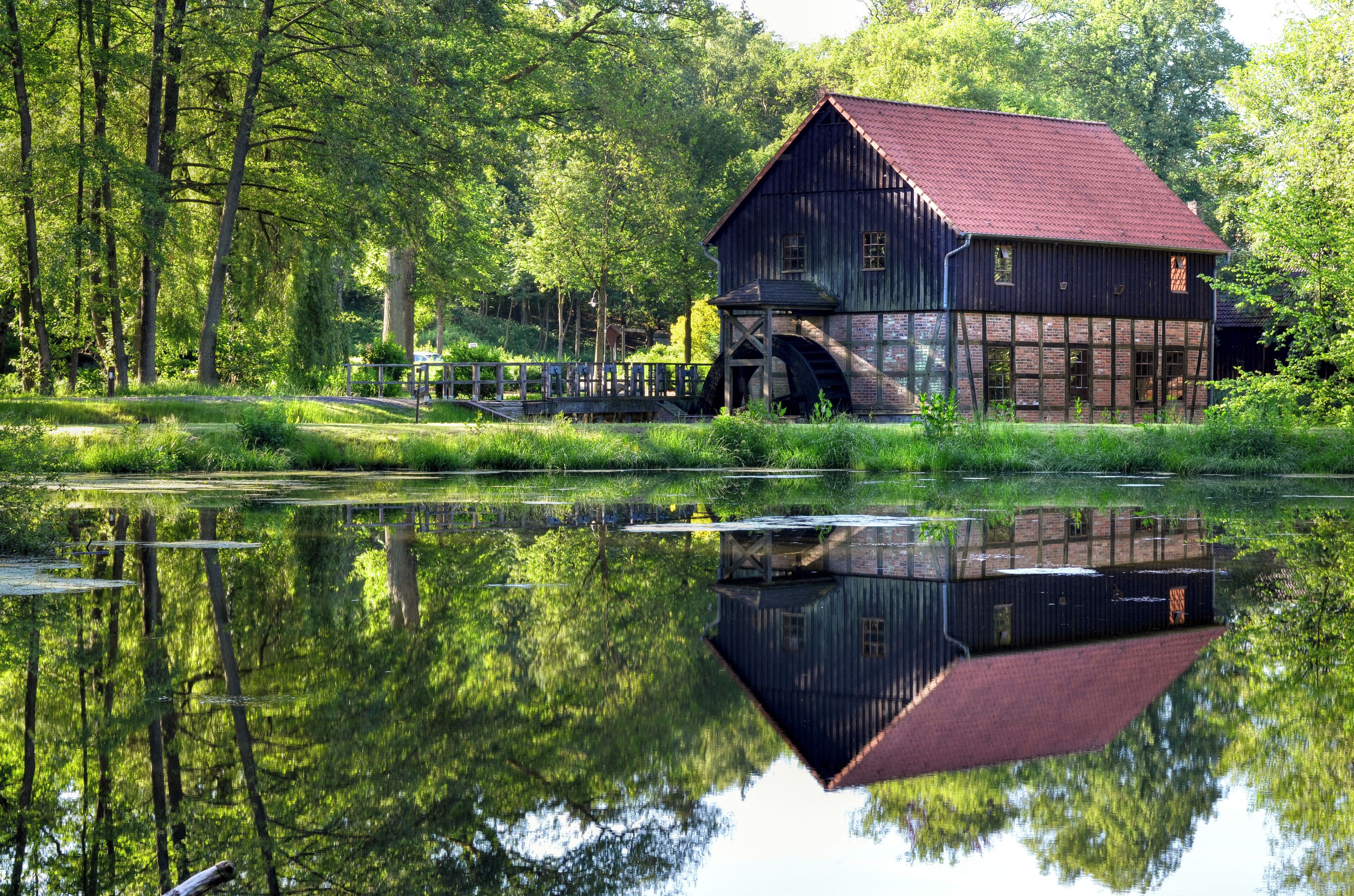 A rustic wooden building with a red roof, a water wheel, and a pond reflecting the structure.
