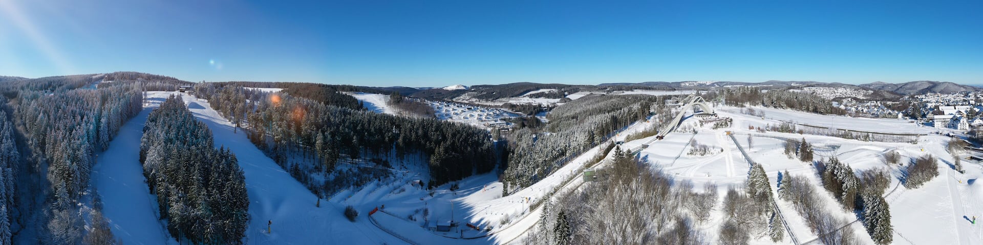 Saint George ski jump and ski slopes of Winterberg ski lift carousel photographed from the air. Panorama image of deserted winter sports area.