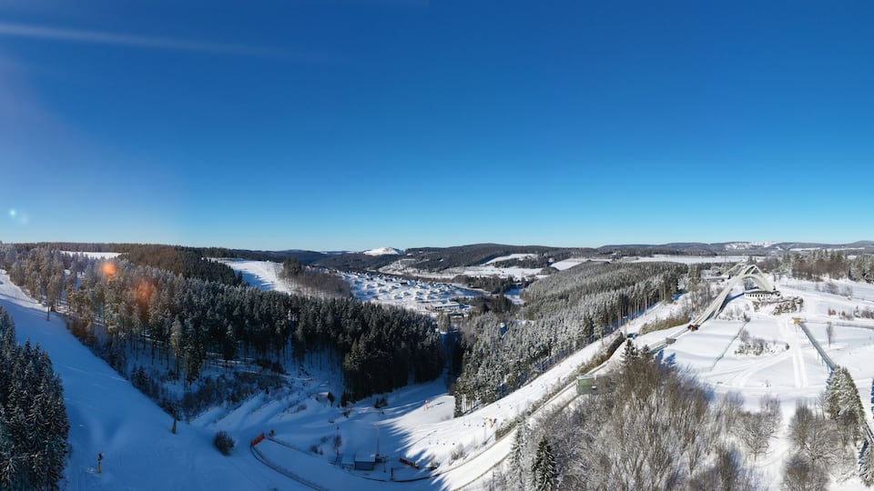 Saint George ski jump and ski slopes of Winterberg ski lift carousel photographed from the air. Panorama image of deserted winter sports area.