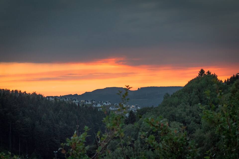 Un atardecer sobre una colina boscosa con un pequeño pueblo en el valle.