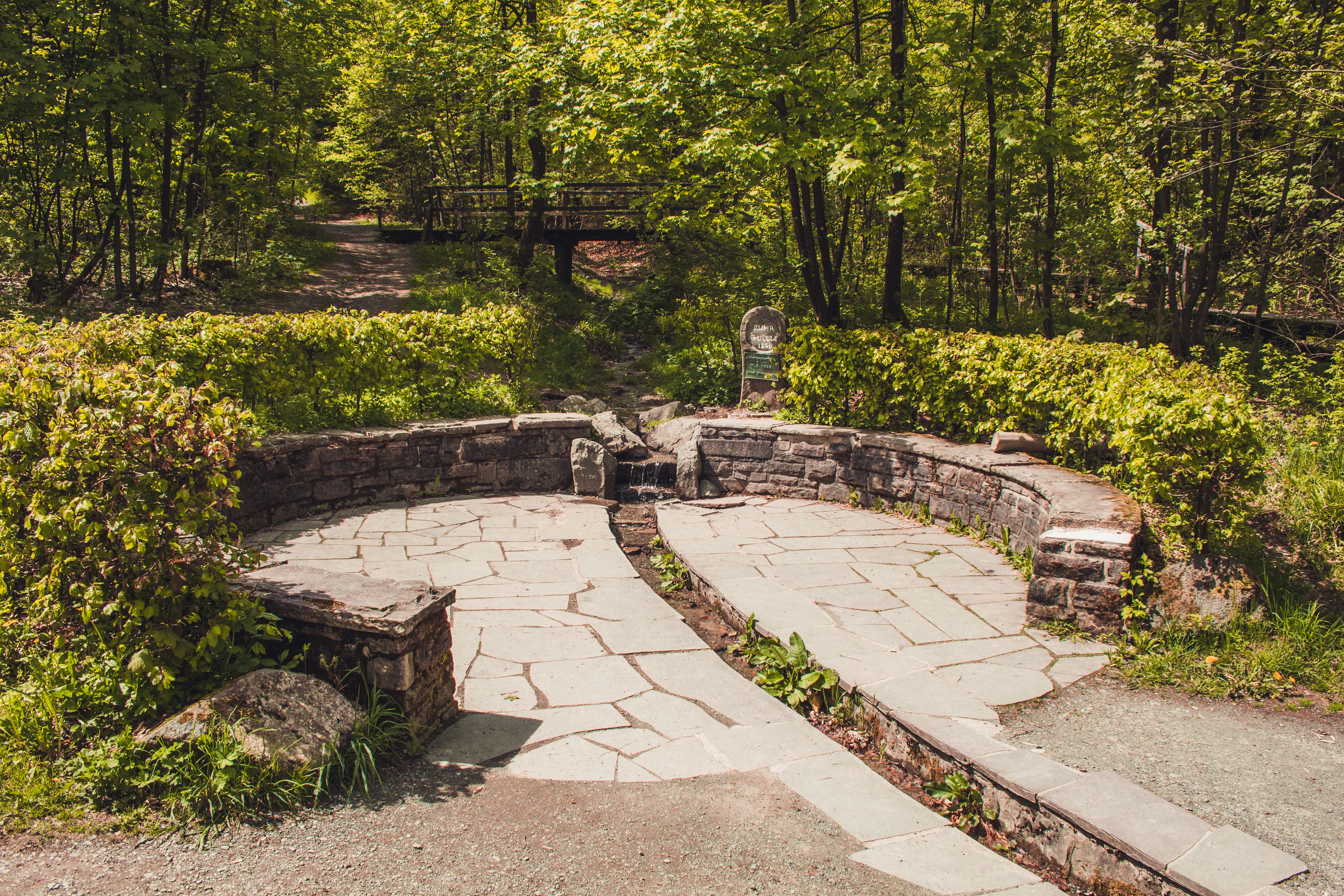 A stone pathway in a park with a circular stone structure, surrounded by lush greenery and trees.