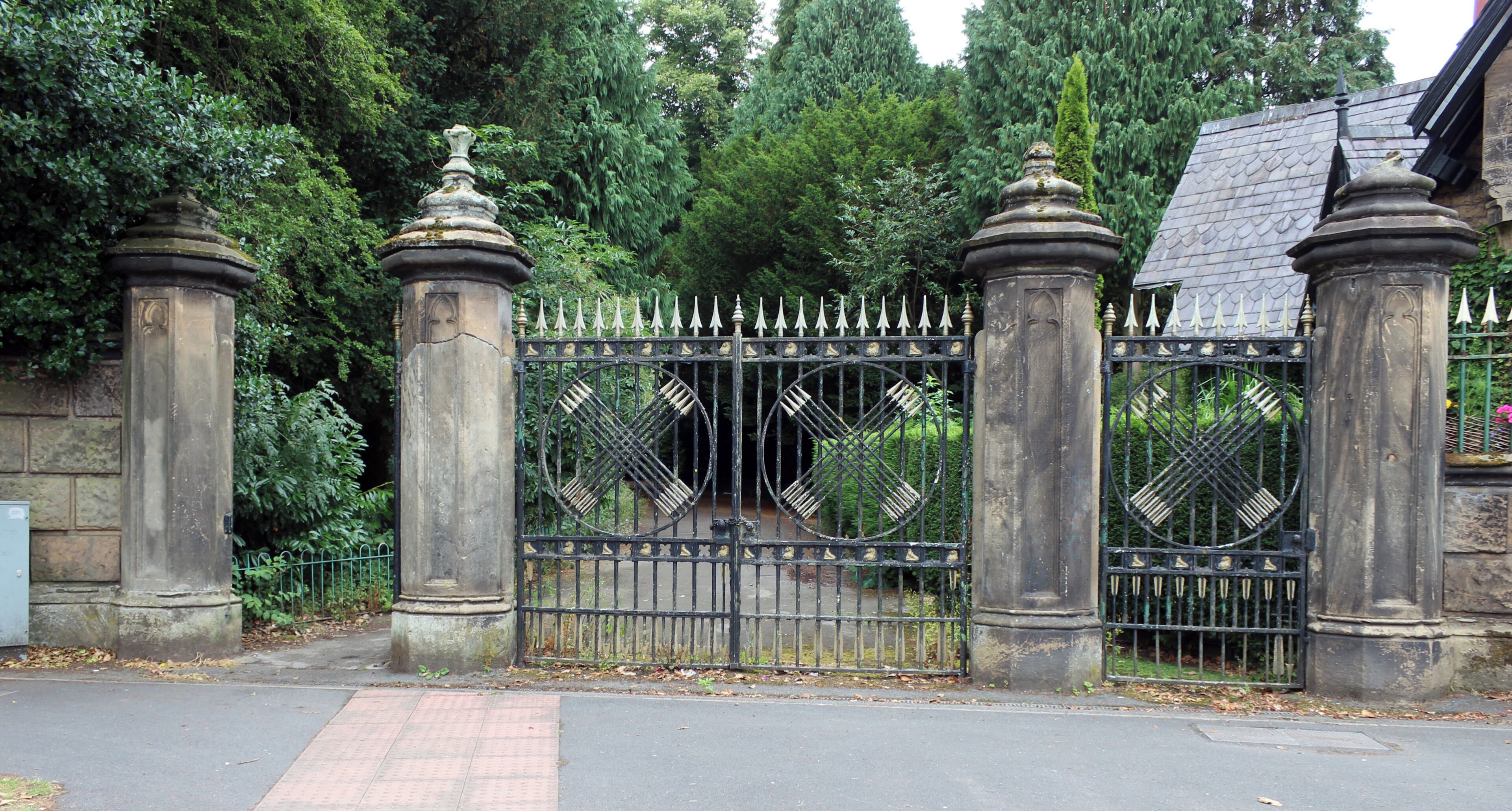 Grade II listed gateway to Arrowe Hall, c. 1835 with ocatagonal piers and cast iron gates with arrow theme.