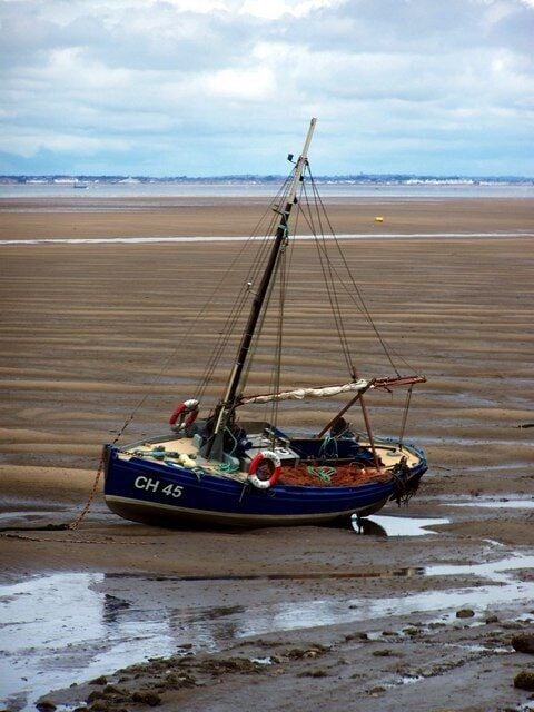 A blue fishing boat with the number CH 45 on a sandy beach with a calm sea in the background.