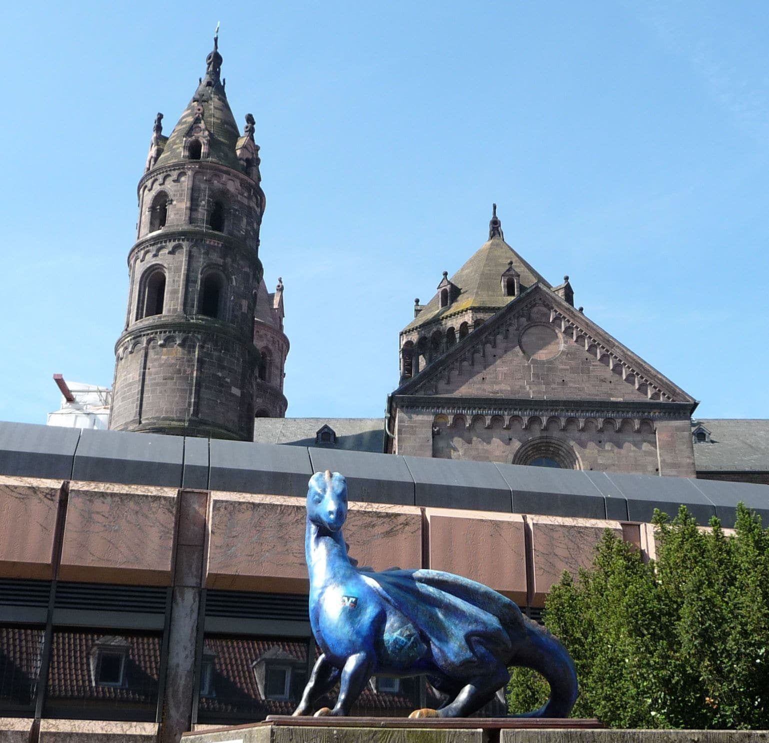A blue sculpture of a horse in front of a historic building with a tower and a dome.