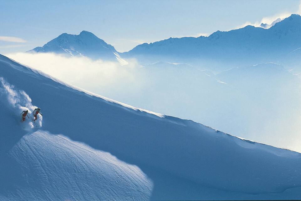 A snowy mountain slope with skiers descending.