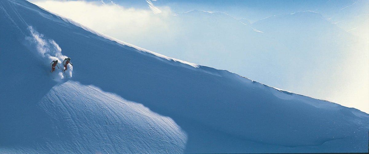 A snowy mountain slope with skiers descending.