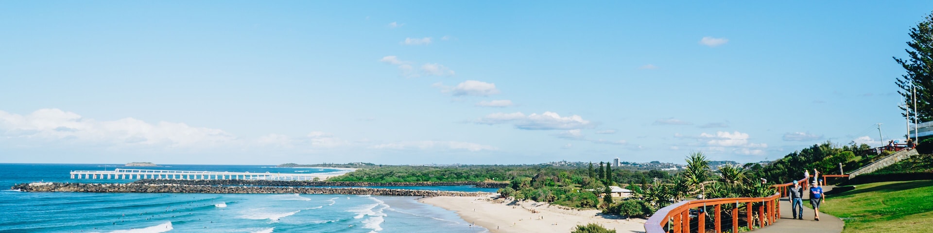 Uma passarela costeira com vista para o oceano, a praia e um píer ao longe.