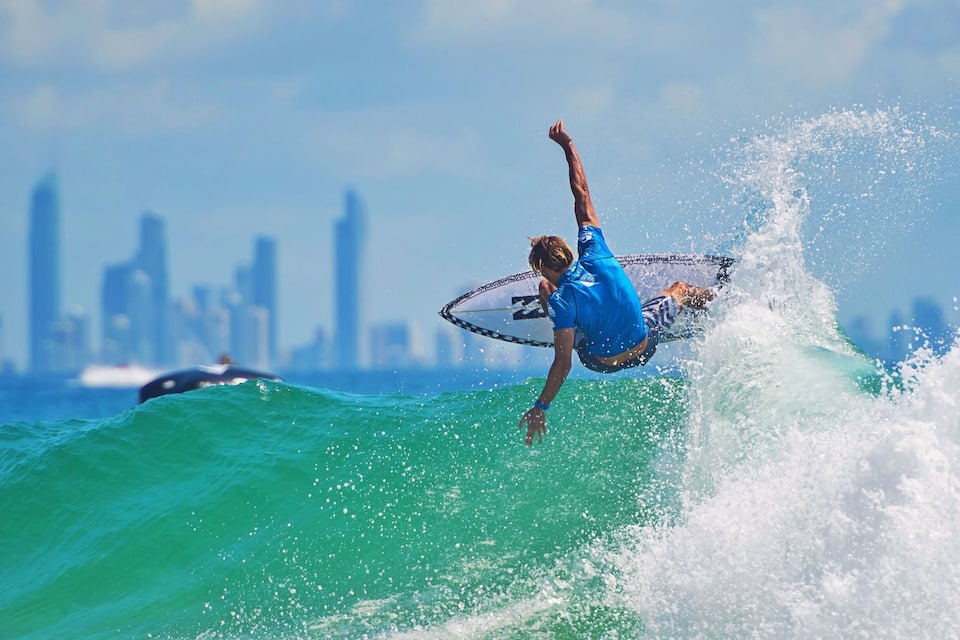 A surfer riding a wave with a city skyline in the background.