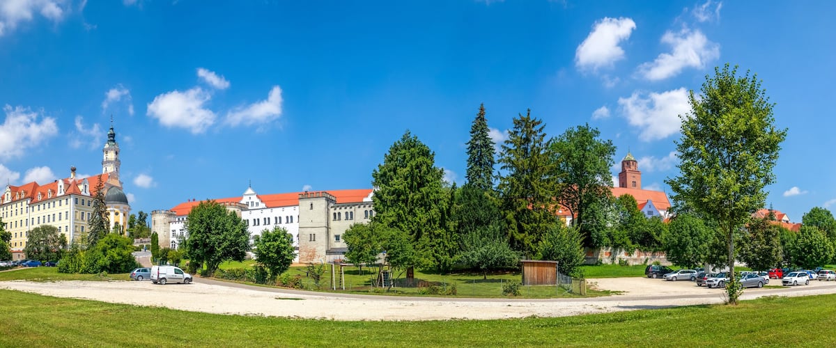 A castle with red roofs, a church with a tall tower, and a parking lot with cars.