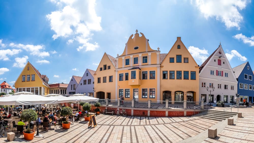 A town square with colorful buildings, outdoor seating, and a clear blue sky.
