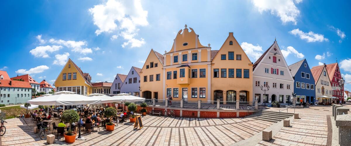 A town square with colorful buildings, outdoor seating, and a clear blue sky.