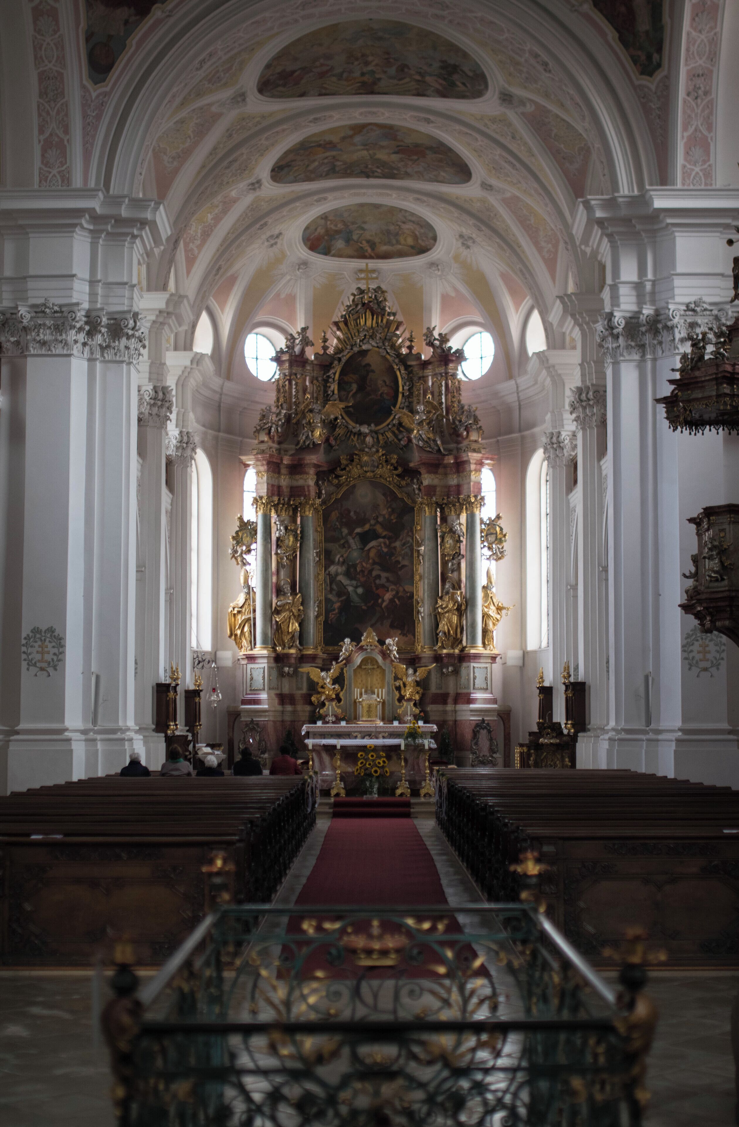 An ornate church interior with a central altar, pews, and a red carpet.